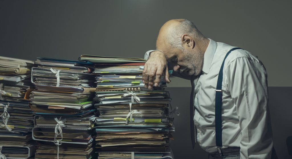 Stressed sad business executive overloaded with piles of paperwork, bureaucracy, taxes and deadlines concept