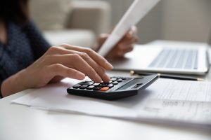 Close up young mixed race woman calculating domestic expenses involved in financial paperwork indoors, focused lady managing monthly banking payments summarizing utility bills and taxes at home.