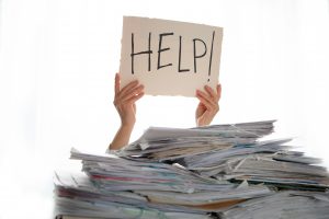 Person under a pile of papers with a hand holding a sign of help. Accounting.